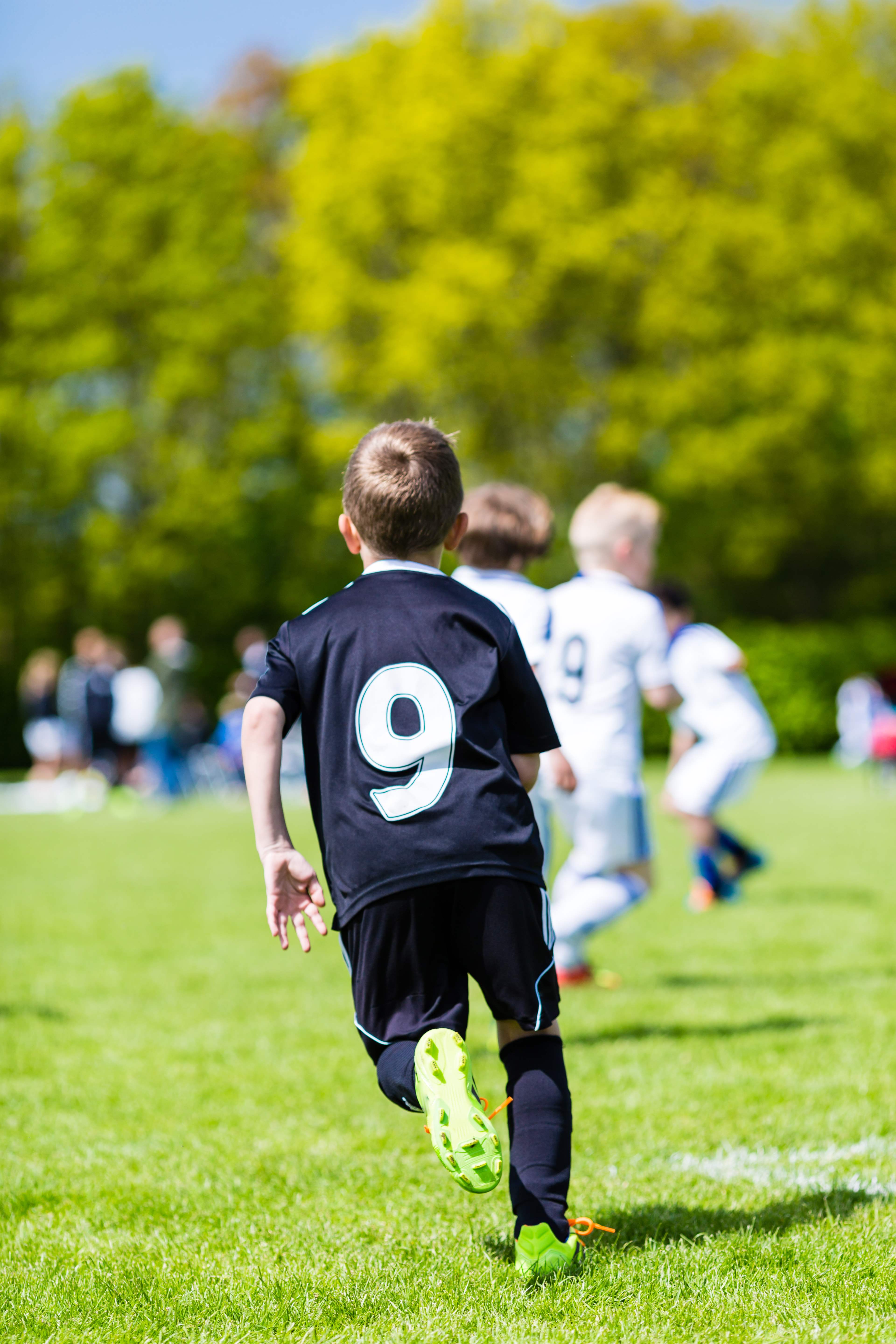 Young boy watching his team mates play a kids soccer match on soccer field with green grass.